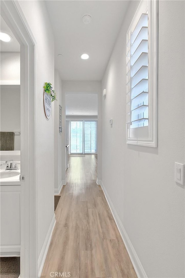 corridor with light wood-type flooring, baseboards, and a sink