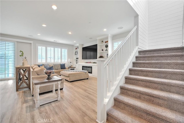 living area with recessed lighting, stairway, a glass covered fireplace, and light wood finished floors