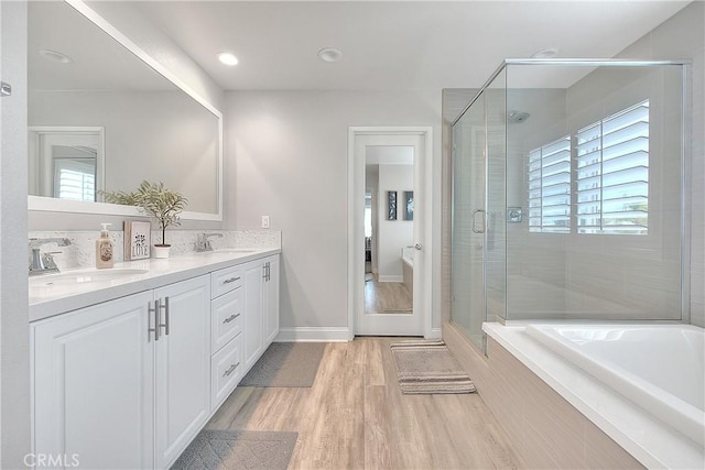 bathroom featuring double vanity, a shower stall, wood finished floors, and a sink