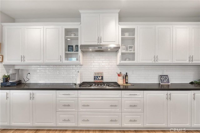 kitchen featuring under cabinet range hood, glass insert cabinets, dark countertops, and white cabinetry