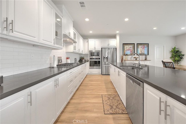 kitchen featuring a sink, under cabinet range hood, dark countertops, white cabinetry, and stainless steel appliances