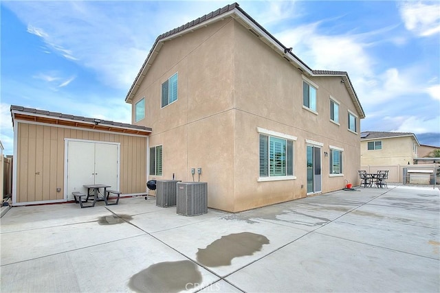 rear view of house featuring central AC unit, stucco siding, a storage shed, an outdoor structure, and a patio