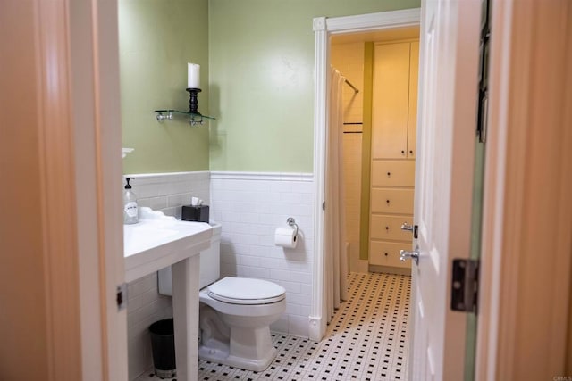 bathroom featuring a wainscoted wall, toilet, tile walls, and a shower with curtain