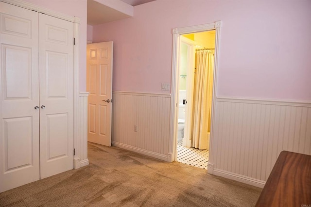 unfurnished bedroom with a closet, a wainscoted wall, carpet flooring, and ensuite bath