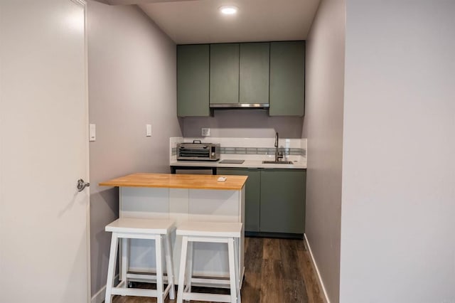 kitchen with a toaster, a sink, baseboards, and green cabinetry