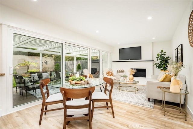 dining area featuring recessed lighting, a fireplace with raised hearth, and light wood-style flooring