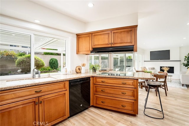 kitchen with light stone counters, brown cabinets, black appliances, and a sink