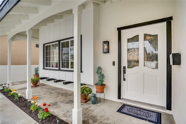 doorway to property with covered porch, board and batten siding, and stucco siding