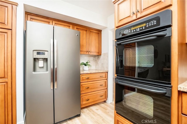 kitchen with tasteful backsplash, light stone counters, light wood-style floors, stainless steel refrigerator with ice dispenser, and dobule oven black