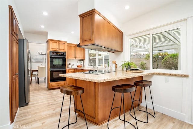 kitchen with light wood-type flooring, black appliances, a peninsula, and a healthy amount of sunlight