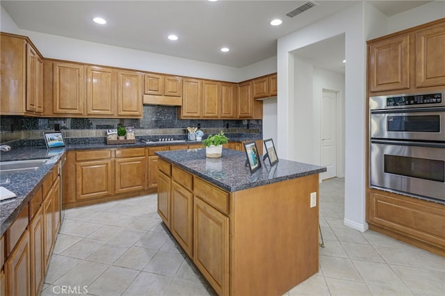 kitchen with visible vents, dark stone counters, under cabinet range hood, appliances with stainless steel finishes, and tasteful backsplash