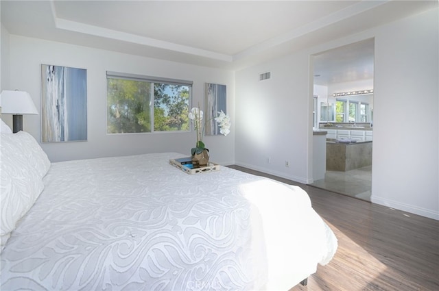 bedroom featuring visible vents, baseboards, a tray ceiling, and wood finished floors