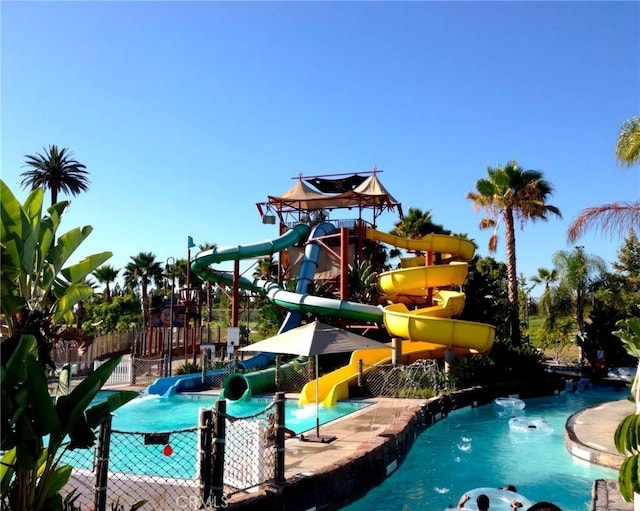 community pool featuring playground community, a water play area, a water slide, and fence