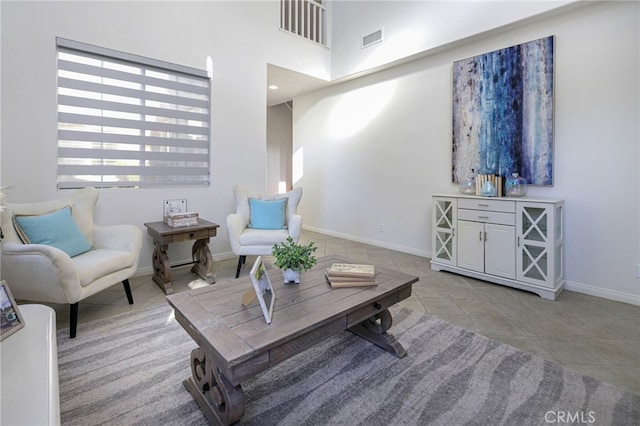 tiled living area featuring visible vents, baseboards, and a towering ceiling