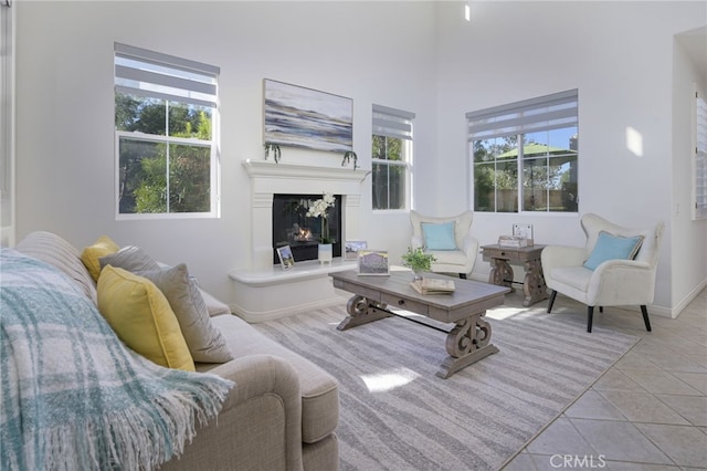 living room featuring a wealth of natural light, a glass covered fireplace, tile patterned flooring, and baseboards