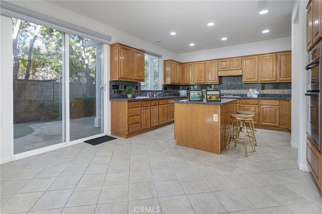 kitchen with backsplash, a center island, a kitchen bar, stainless steel gas stovetop, and brown cabinetry