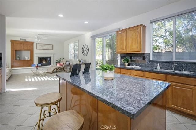 kitchen with light tile patterned floors, a ceiling fan, visible vents, decorative backsplash, and a glass covered fireplace