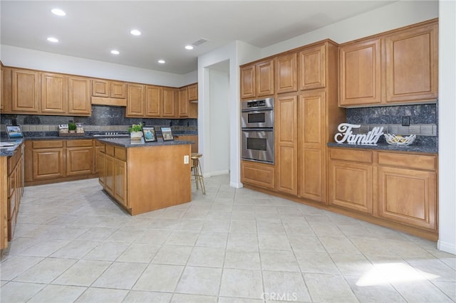 kitchen with visible vents, a kitchen island, under cabinet range hood, appliances with stainless steel finishes, and brown cabinets