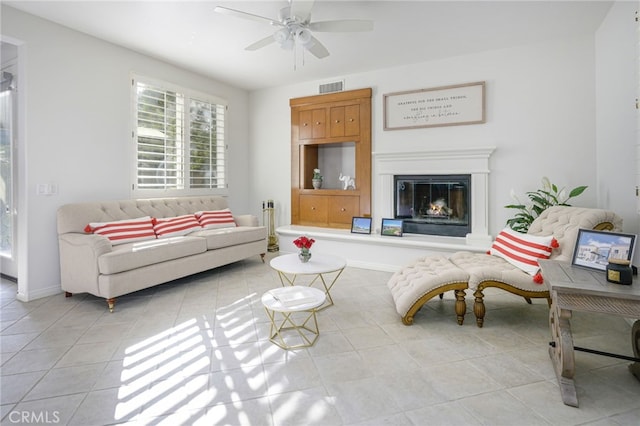 living area featuring light tile patterned floors, a ceiling fan, visible vents, baseboards, and a glass covered fireplace