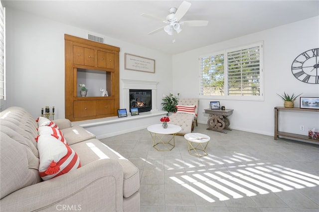 tiled living room with a glass covered fireplace, baseboards, visible vents, and ceiling fan