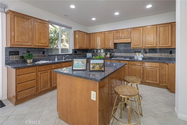 kitchen with a kitchen island, under cabinet range hood, a breakfast bar area, stainless steel gas stovetop, and brown cabinetry