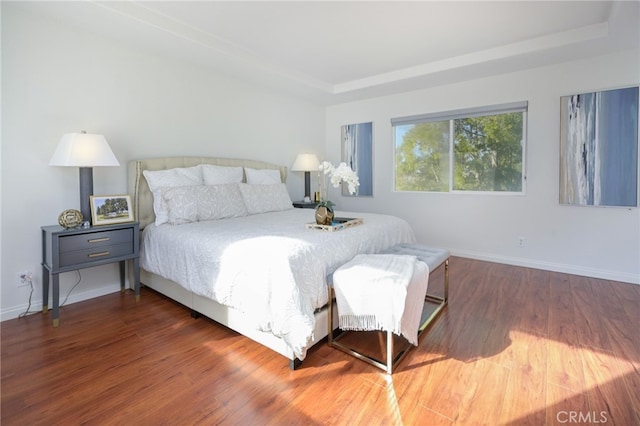 bedroom featuring a raised ceiling, wood finished floors, and baseboards