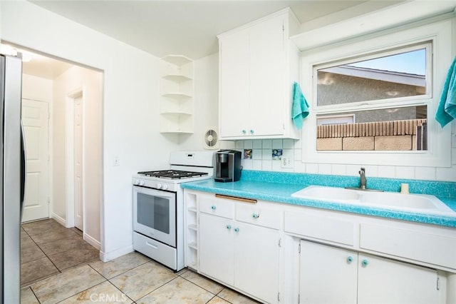 kitchen with a sink, gas range gas stove, freestanding refrigerator, white cabinets, and open shelves