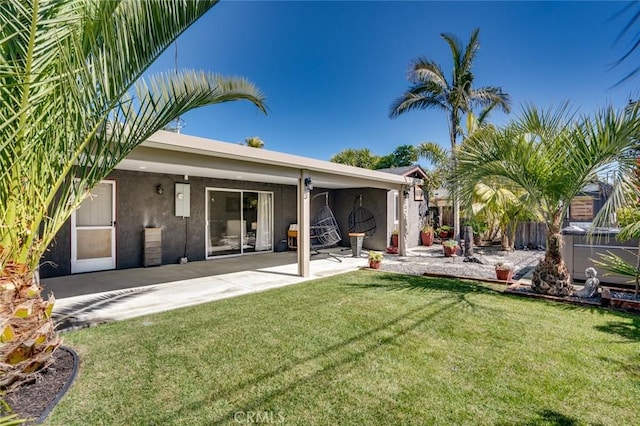 rear view of house with a patio area, a lawn, fence, and stucco siding