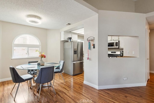 dining area featuring baseboards, wood finished floors, visible vents, and a textured ceiling