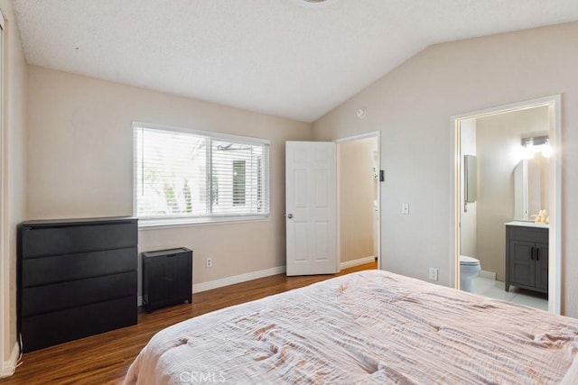 bedroom with baseboards, lofted ceiling, wood finished floors, and ensuite bathroom