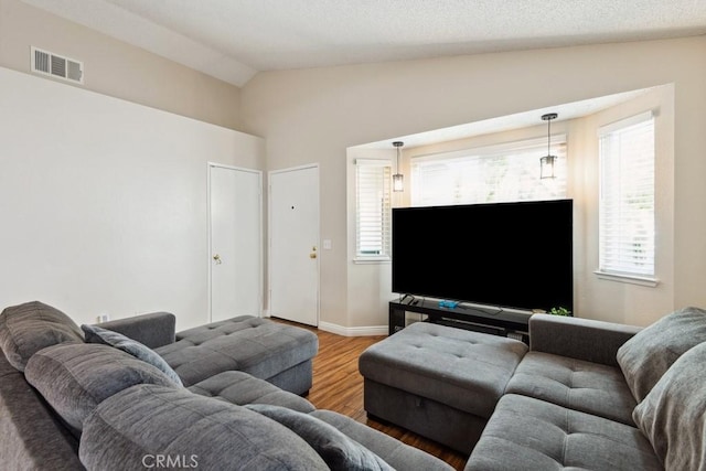 living room featuring visible vents, wood finished floors, baseboards, and vaulted ceiling