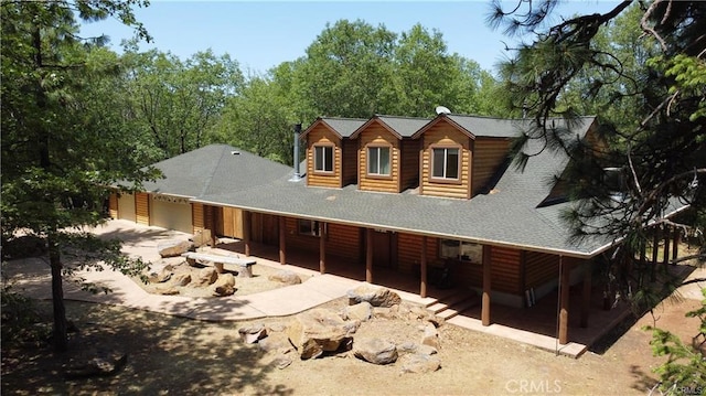 rear view of house with log veneer siding, covered porch, roof with shingles, and an attached garage