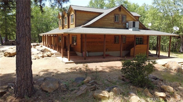 back of property with a carport, log veneer siding, and roof with shingles