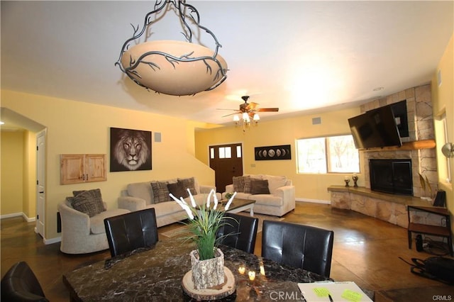 dining area with arched walkways, a fireplace, a ceiling fan, and baseboards