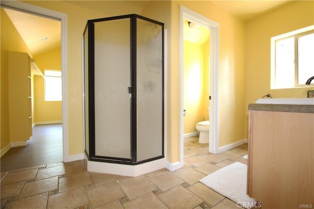 bathroom with baseboards, toilet, stone tile floors, and a shower stall