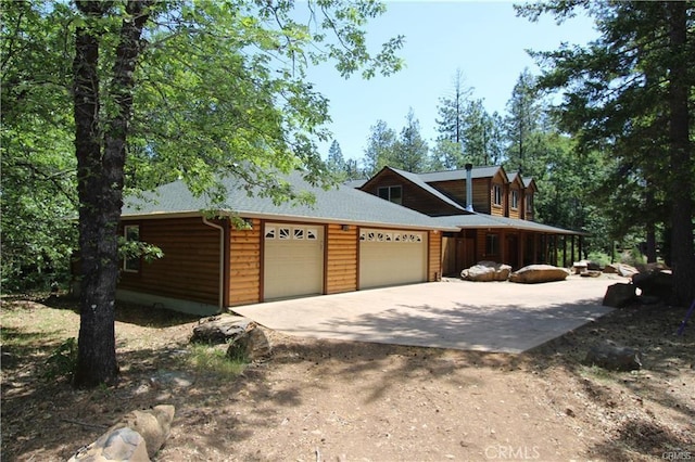 view of side of home featuring an attached garage, driveway, and a shingled roof