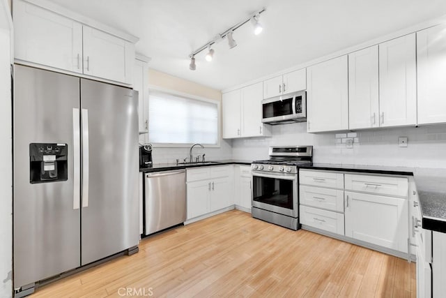 kitchen featuring light wood-type flooring, decorative backsplash, stainless steel appliances, white cabinetry, and a sink