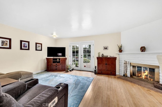 living room with a glass covered fireplace, french doors, baseboards, and wood finished floors