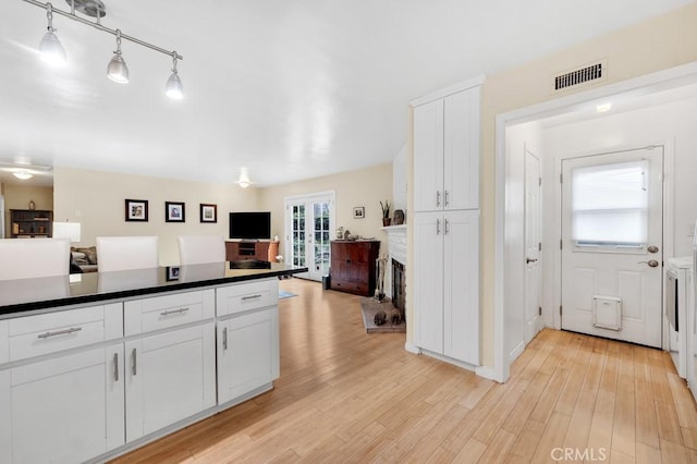 kitchen with visible vents, open floor plan, white cabinets, a fireplace, and light wood finished floors