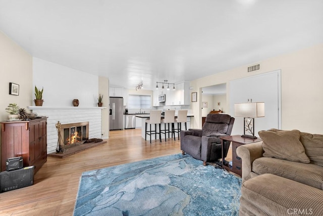 living room featuring light wood finished floors, visible vents, and a fireplace