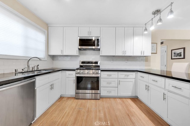 kitchen with a sink, stainless steel appliances, light wood-style floors, and white cabinetry