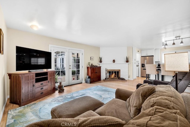 living room with track lighting, a brick fireplace, french doors, and light wood finished floors