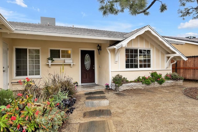 entrance to property featuring stucco siding, fence, and a shingled roof