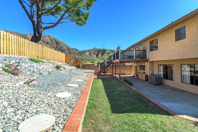 view of yard with a deck with mountain view, a fenced backyard, cooling unit, stairway, and a patio area