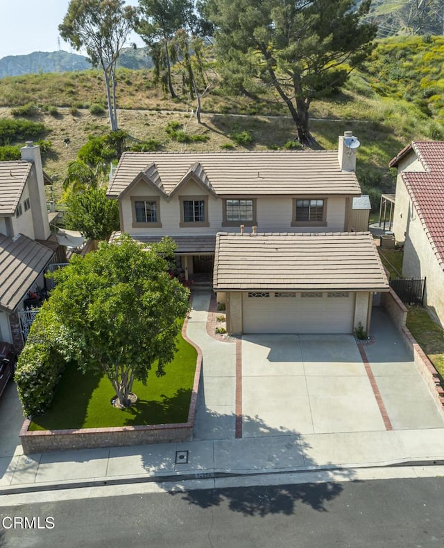 traditional-style home featuring driveway, a tile roof, a mountain view, a garage, and a chimney