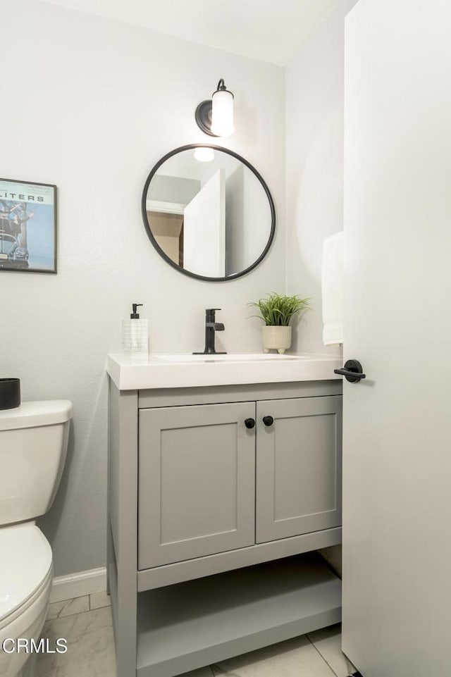 half bathroom featuring vanity, toilet, baseboards, and marble finish floor