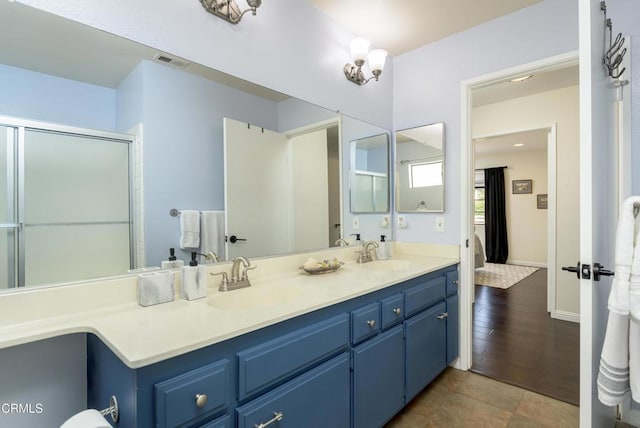 full bathroom featuring double vanity, visible vents, a shower with door, and a sink