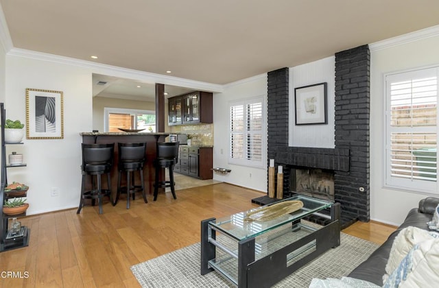 living room with a fireplace, light wood-style floors, and ornamental molding