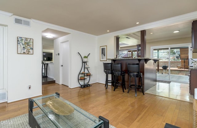 living room with crown molding, light wood-style floors, and visible vents