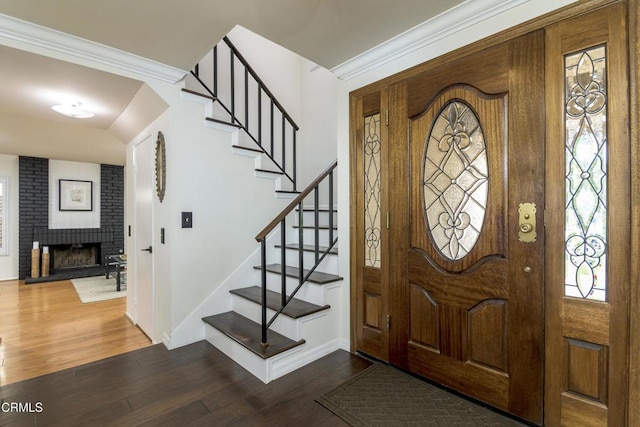 entrance foyer with a brick fireplace, baseboards, stairs, ornamental molding, and wood finished floors